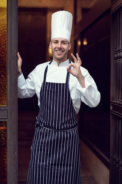 Koch steht im Eingang seines Restaurants in München, authentische Businessfotografie für Gastronomie
