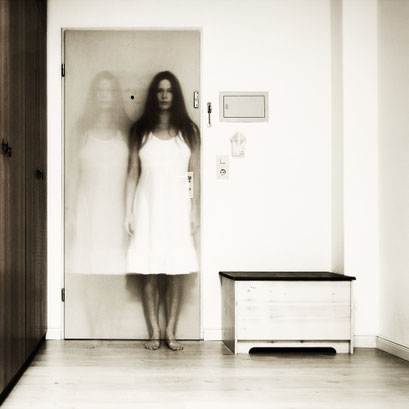 Manuela Deigert Fotokunst Start, Multiple, Langzeitbelichtung eines Selbstportraits in doppelter Ansicht, stehend in einem Raum vor einer Tür, seitlich jeweils eine Holzkiste und Schrank