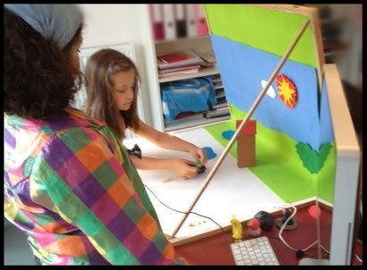 Twee kinderen staan bij een tafel met animatie studio, het meisje verplaatst een kleipoppetje.