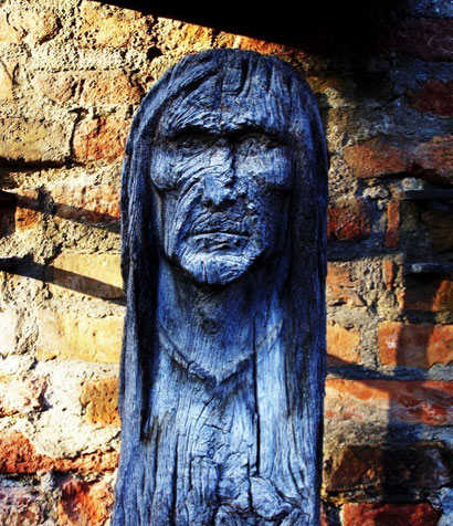 Die atmosphärische Holzfigur der Hexe vom Hexenbrunnen in Augsburg, geschnitzt mit markanten Gesichtszügen und tiefblauer Patina. Ein verborgener Freizeittipp für Touristen und Einheimische auf der Tour „Zwielichtige Gestalten“.