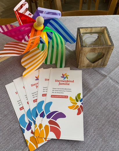 Buntes Windrad, Flyer von Sternenkindfamilie, und Windlicht auf einem Tisch