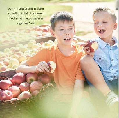 Zwei Jungs sitzen auf einem Traktor voller Äpfel und lassen sich die Äpfel schmecken