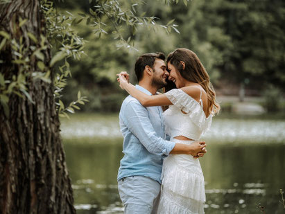 Im Bild ein Paar, das sich umarmt, lächelt sich an - steht an einem Bach in der Natur