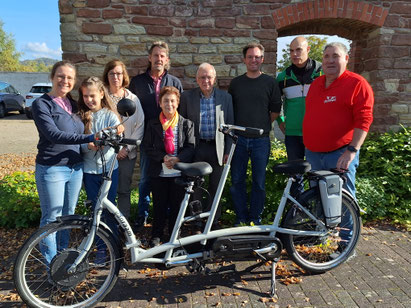 Elisa (2. von links) freut sich bei der Spendenübergabe riesig über das neue Tandem, mit dem sie mit Mama oder Papa durch die Natur sowie u.a. zur Schule und zu Therapien fahren kann.