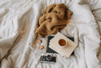 ベッドの上に置かれた本と紅茶のマグカップ。毛糸のストール。カメラとクルミ。