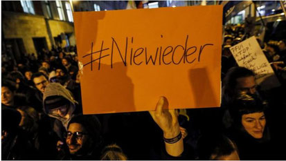 protestors holding a sign that says in German #Niewieder which means never again