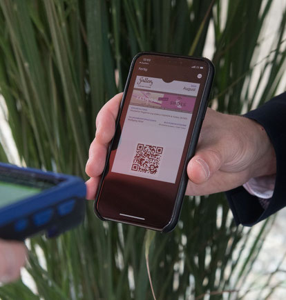 Eine Hand hält ein Smartphone und präsentiert einen QR-Code. Ein Scanner scannt den Code.