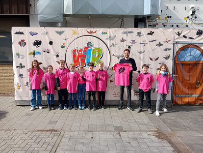 Kinder der SV-AG tragen pinke Shirts. Schulleiter hält auch ein pinkes Shirt hoch