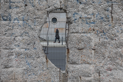 A pedestrian can be seen through a hole in the rest of the Berlin Wall