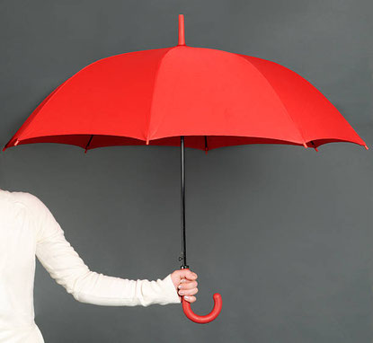 Zur Hälfte sichtbare Person in weiß hält roten geöffneten Regenschirm vor eine graue Wand.