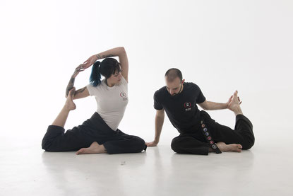 Ein Mann und eine Frau sitzen auf dem Boden und machen Yogapositionen, sie dehnen sich