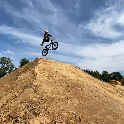 Ein Junge auf einem BMX befährt den Dirtpark und macht einen Sprung auf einer Rampe.