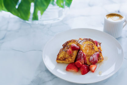 いちごがあしらわれたフレンチトーストのお皿。コーヒーの入ったマグカップ。ガラスの花瓶に生けられたグリーン。