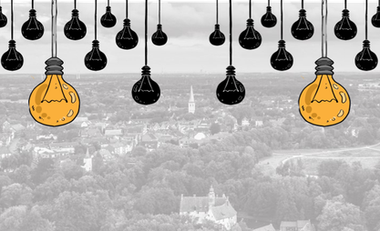 Im Hintergrund ist ein Blick auf die Stadt gegeben. Im Vorderund hängen schwarze und zwei große gelbe Glühbirnen.