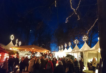 Beleuchtete, weiße Pagodenzelte auf einem Weihnachtsmarkt, mit vielen Besuchern.