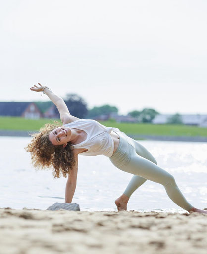 So geht Leichtigkeit: Gut gelaunte Frau übt entspannt und lachend Yoga am Strand. 