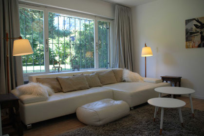 Fernseh und Loungezimmer mit großer weißer Couch und Blick in den Garten