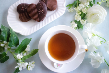 デスクに広げられた4月のカレンダーとピンク色のボールペン。ピンクのバラの花。コーヒーの入ったピンクのマグカップ。