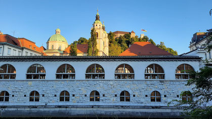 Die lange Markthalle an der Ljubljanica mit Burg im Hintergrund