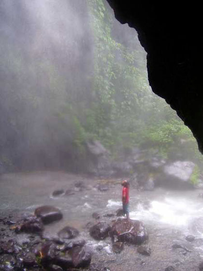 Auf einem Felsblock mitten im Bergbach steht ein Mann und betrachtet den Wasserfall