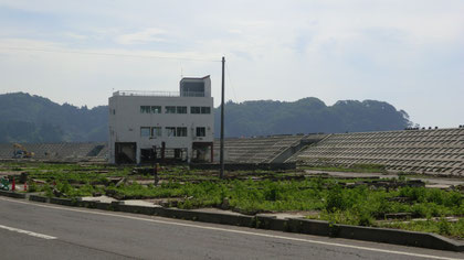 国道から防波堤を望む。手前の建物は鉄筋部分だけのこった農協跡。手前の草むした所がかつて家屋があった場所。礎石のみが残っていた