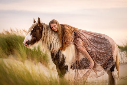 Frau mit Glitzerkleid sitzend auf Pferd mit langer Mähne in den Dünen am Strand Fotoshooting im Abendlicht
