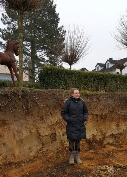 Lebensgröße Yvonne - sie steht im zukünftigen Reitplatz, im Hintergrund die Einfahrt.