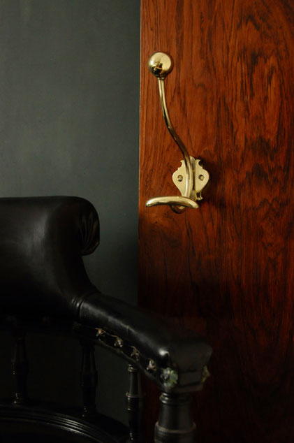 Patère double crochets pour vêtements et accessoires en laiton doré poli dans un décor élégant composé de panneau mural en bois, fond vert anglais et fauteuil de bureau ancien anglais en cuir noir