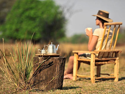 Mujer con sombrero sentada de espaldas en el campo tomando un té