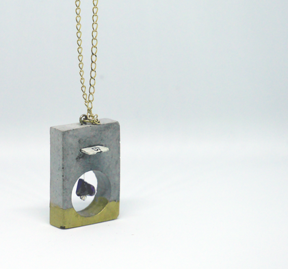 Pendentif rectangulaire en béton avec bande doré inférieure, extrudé en arrondi. Présence d'une améthyste dans l'extrusion. Au dessus, encoche fine avec papier contenant une affirmation positive. Chaine couleur or