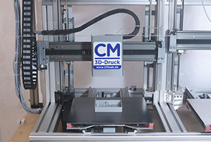 Eigenentwickelter 3D-Drucker. Konstruktion Aluprofile. Schwarzes Druckbett auf zwei Schienen vor und zurück fahren. Druckkopf einer Schiene links und rechts fahren. Links/rechts Gewindespindeln für hoch runter. Kabel links.
