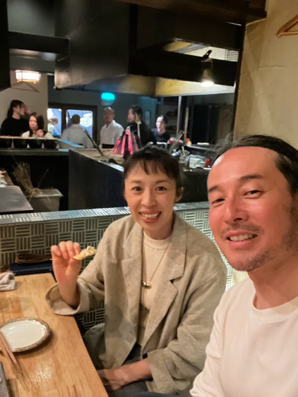 山口県の金魚という雰囲気がいい炭火焼き居酒屋にて夫婦で夕食を楽しむ様子で男性は白いTシャツを着ていて、女性はベージュのジャケットを羽織りクラッカーを手に持っています。