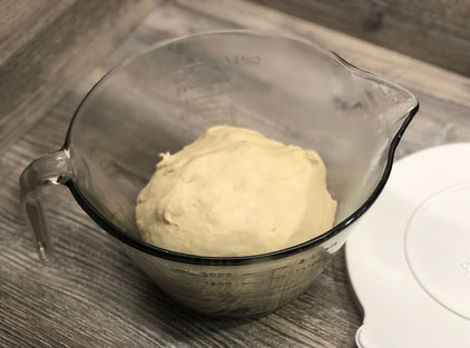 Glasbehälter mit Hefeteig auf Holztisch stehend