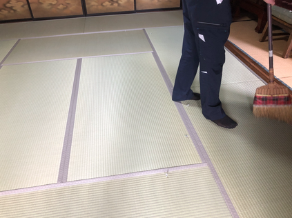畳の目に沿ってほうきで丁寧に仕上げ掃除をするスタッフの様子