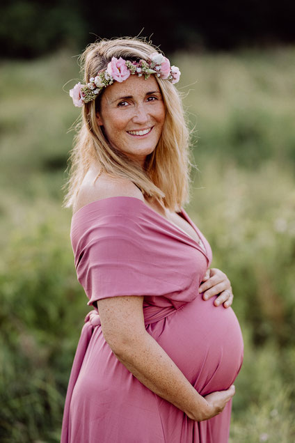 Halbportrait einer schwangeren Frau in rosafarbenem Kleid, von der Seite aufgenommen