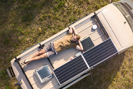 Mann liegt auf dem Dach vom Camper Van mit Solaranlage