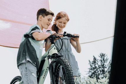 Zwei Kinder stehen an einem R Raymon Kinder e-Bike
