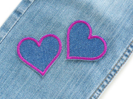 2 blaue Jeansflicken in Herzform mit lila Umrandung sind als Hosenflicken auf eine Jeanshose aufgebügelt