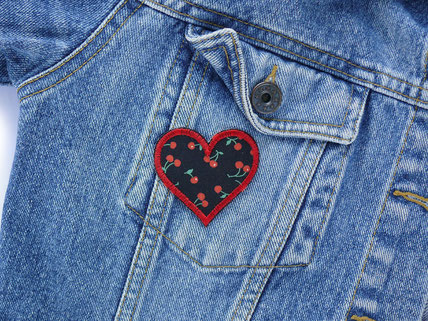 ein kleiner Herz Aufnäher mit Kirschen wurde als Accessoire auf eine blaue Jeansjacke gebügelt