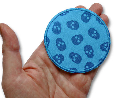 runder Bügelflicken mit blauen Totenköpfen liegt auf einer Hand