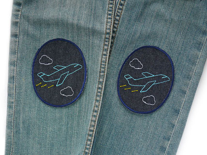 !B Ein ovaler Jeansflicken mit aufgesticktem Flugzeug wurde zum Reparieren von einem Hosenloch auf eine Kinderhose gebügelt