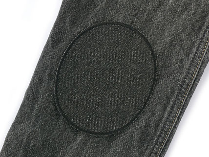 ein schwarzer Flicken aus robustem Jeansstoff repariert ein Loch in einer schwarzem Jeanshose