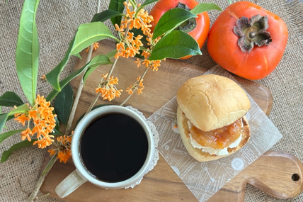 ジャムとチーズがサンドされたパン。コーヒーの入ったマグカップ。キンモクセイの小枝と柿。