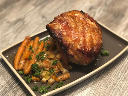 Schweinebraten auf grauer Servierplatte angerichtet