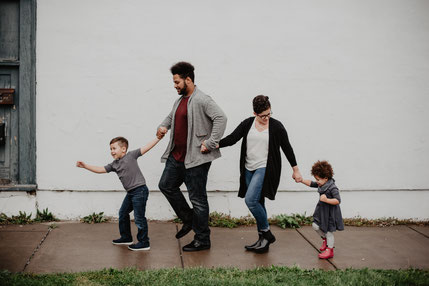 Familie mit 2 Kindern Hand in Hand auf dem Bürgersteig