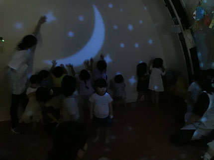 最後は、壁や床にプラネタリウムを映して遊びました。お部屋の電気を消すと「わぁ！おほしさま、いっぱい！」「きれい！」と歓声が上がり、みんな壁や床をタッチしたり、ジャンプしたりして、「おほしさま、つかまえた！」「おつきさま、さわれた！」と楽しんでいました。