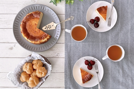 ホールサイズのチーズケーキがカットされたサクランボが添えらえたお皿に取り分けられている。シュークリームが盛り付けられた籐のかご。