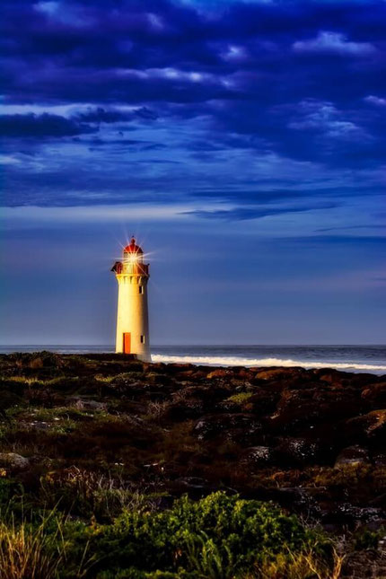 Ein Leuchtturm an einem idyllischen Strand - in der Dämmerung, das Licht ist schon an