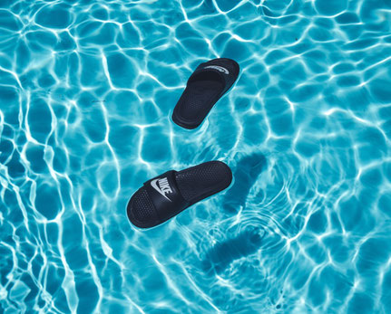 Auf der Wasseroberfläche eines Pools treiben schwarze Badeschlappen.