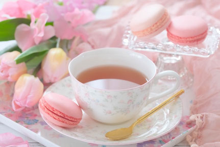 ピンク色のマカロンが添えられた紅茶のカップ＆ソーサ。ピンク色のチューリップ。